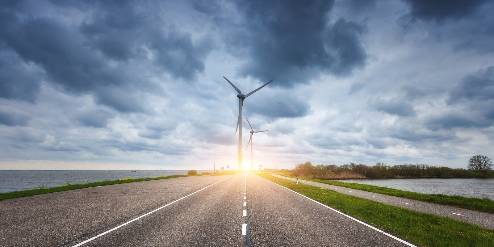 Beautiful asphalt road with wind turbines generating electricity at sunset. Windmills for electric power production. Landscape with road, green grass and wind mills and blue cloudy sky in spring
