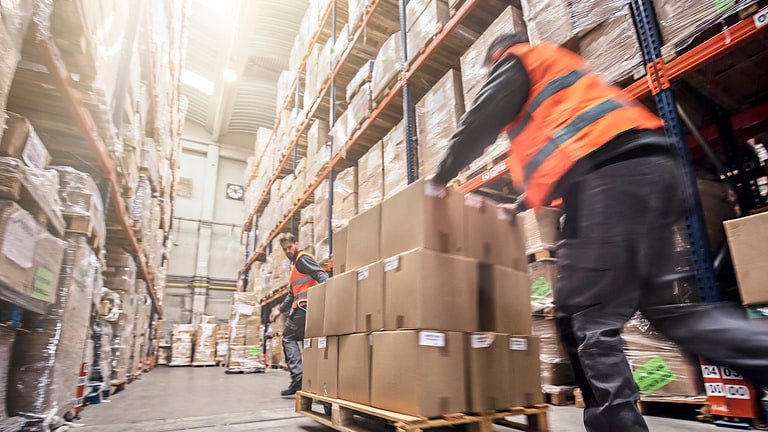Motion blur of two men moving boxes in a warehouse.