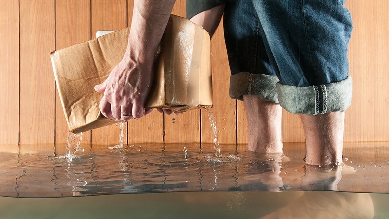 Man lifting cardboard box in flooded basement, low section