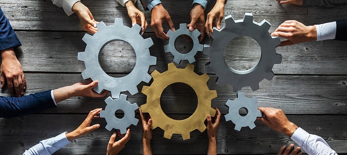 Group of business people joining together silver and golden colored gears on table at workplace top view
