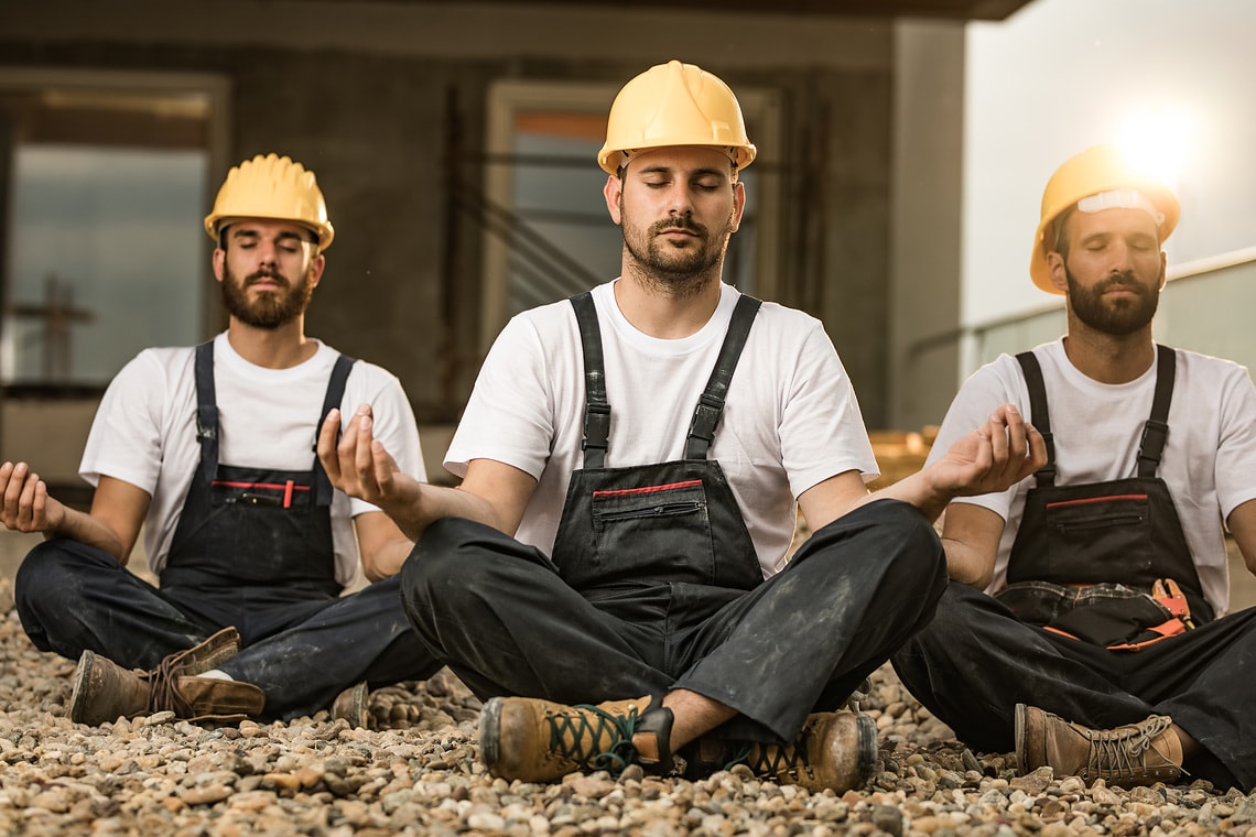 Group of construction workers exercising Yoga in Lotus position during a break at balcony.