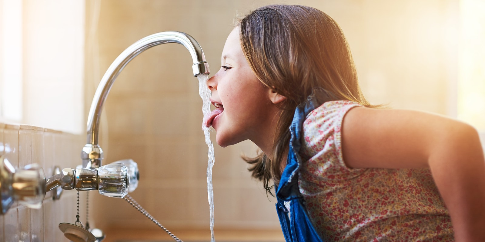 Aufnahme eines kleinen Mädchens, das zu Hause Wasser direkt aus dem Küchenhahn oder Armatur trinkt