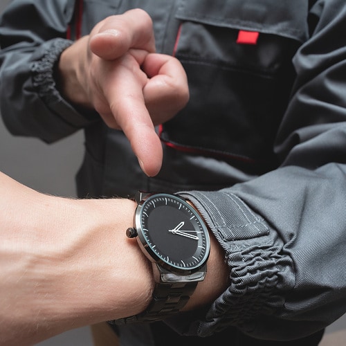 Car service worker is pointing on the wrist watch on his hand close up. Fast service.