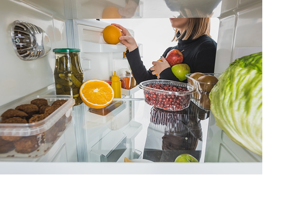 abgeschnittene Ansicht einer Frau, die reife Früchte aus dem Kühlschrank nimmt, mit Lebensmitteln isoliert auf weiß