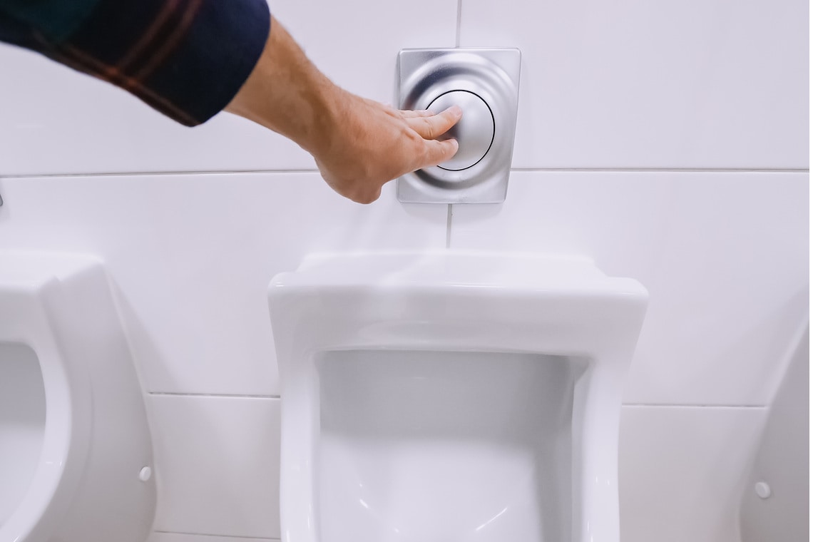 Male hand flashing water in urinals in a public men's toilet. The concept of sanitary cleaning and urology and kidney disease