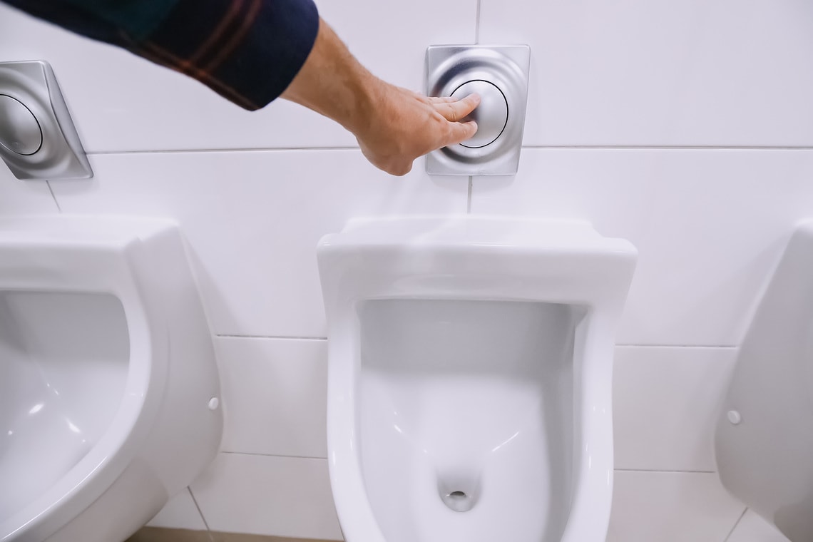 Male hand flashing water in urinals in a public men's toilet. The concept of sanitary cleaning and urology and kidney disease