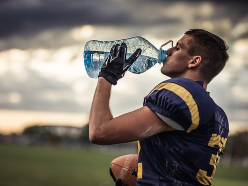 Profile view of young American football player drinking water on a break at playing field.