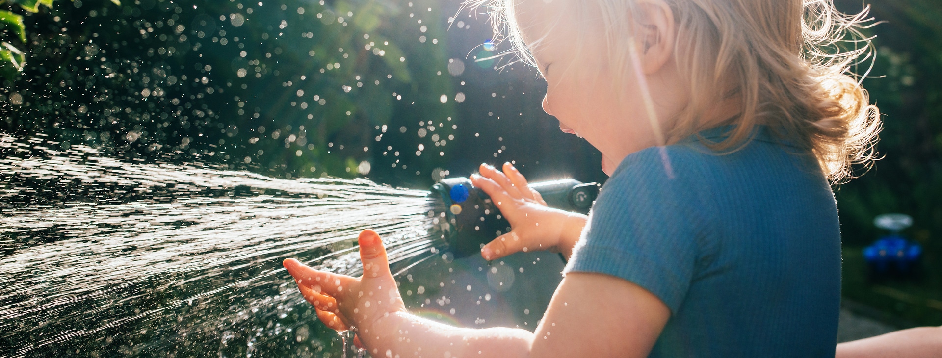 Mother and her happy toddler girl having fun while sprinkling the garden.