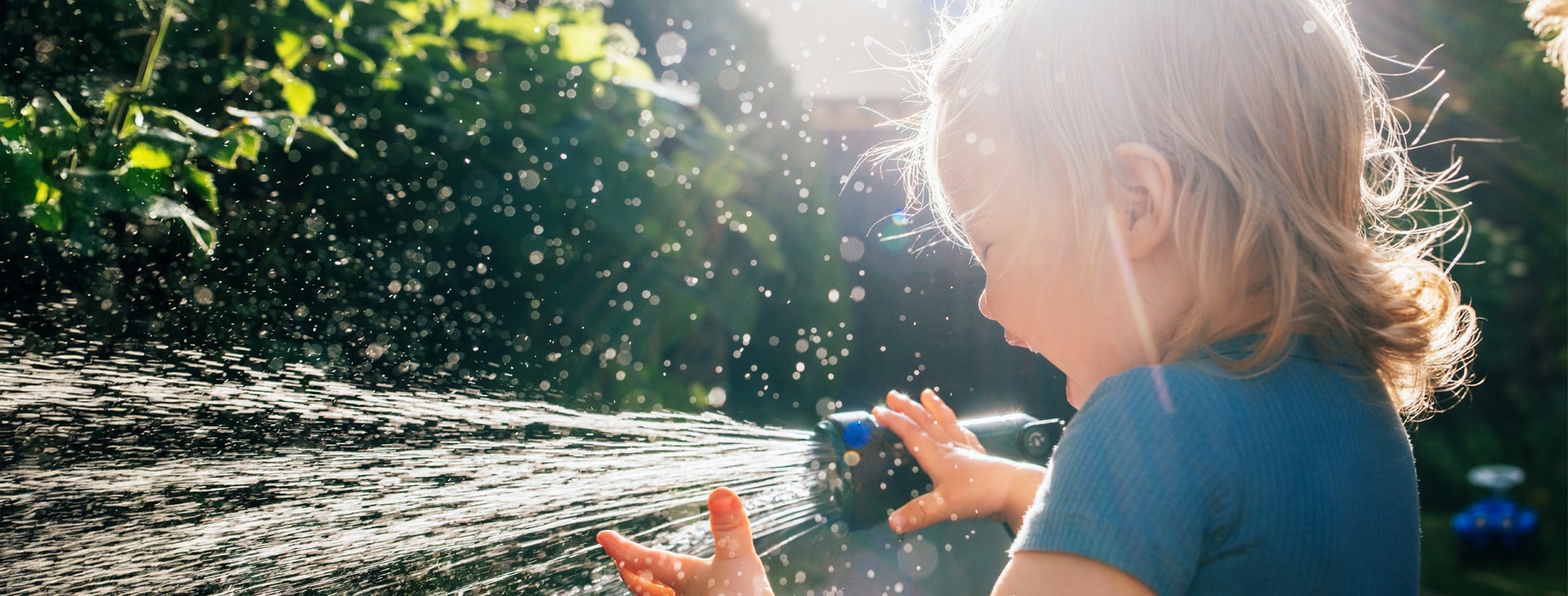 Un enfant joue dans le jardin avec un tuyau d'arrosage