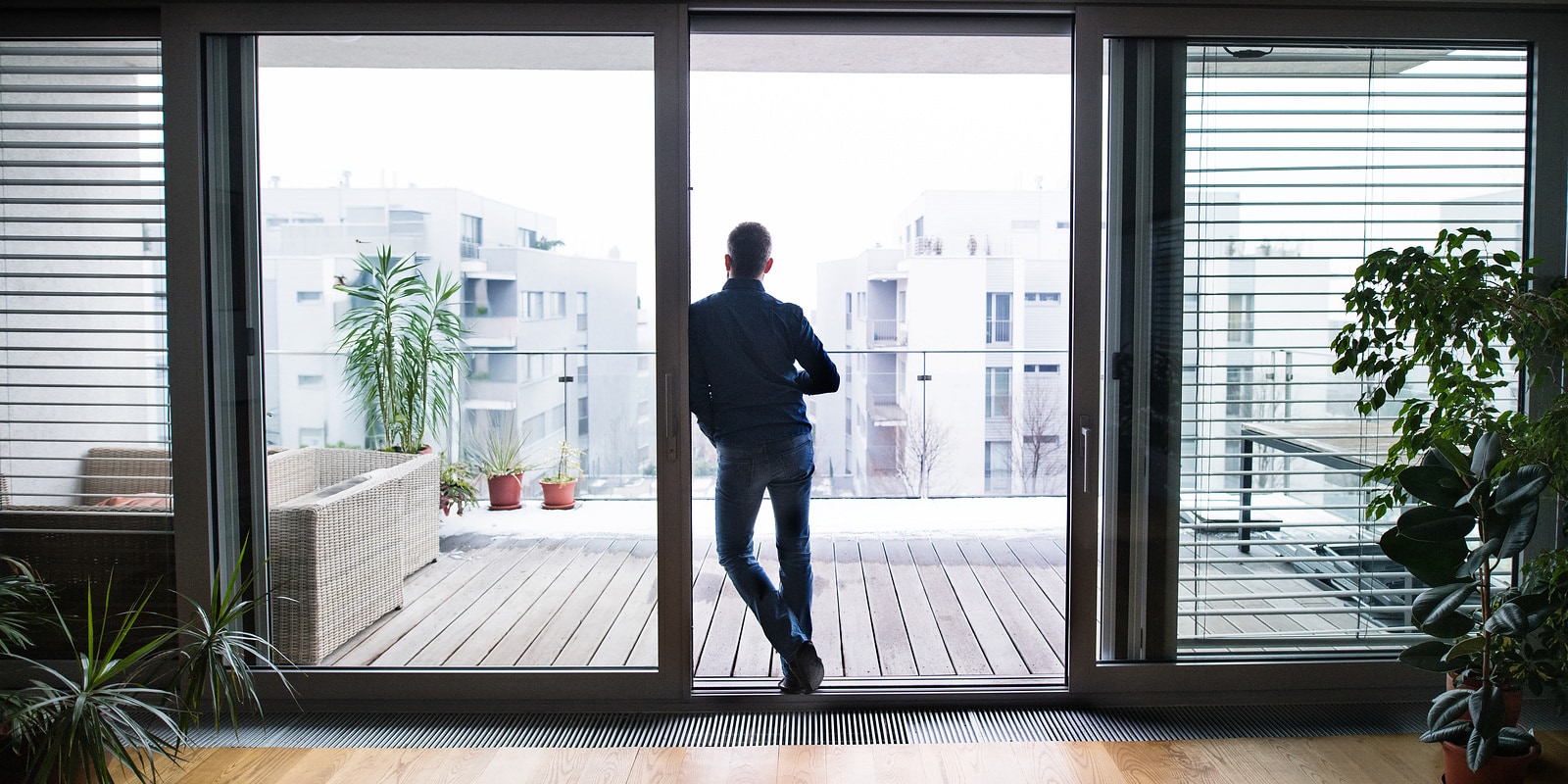 Ein Mann steht auf dem Balkon eines Mehrfamilienhauses und blickt über mehrere benachbarte Wohngebäude im Quartier – sinnbildlich für moderne, zukunftsfähige Lösungen im Bestand sowie für professionelles Immobilien- und Gebäudemanagement.