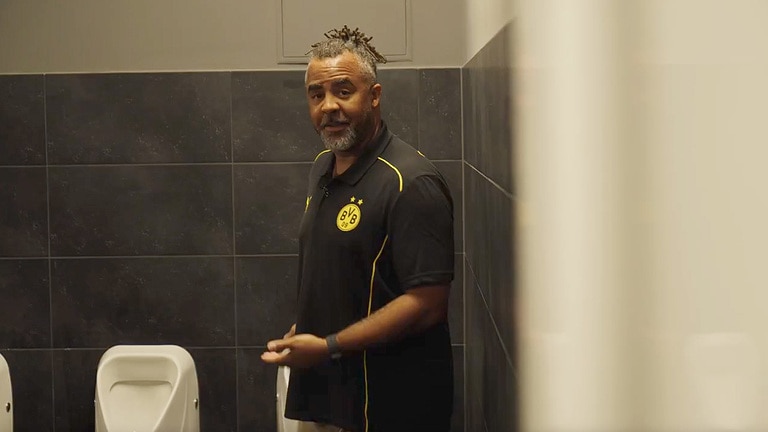 Patrick Owomoyela zwraca uwagę na nowoczesny system odprowadzania wody zanieczyszczonej i ścieków w SIGNAL IDUNA PARK.