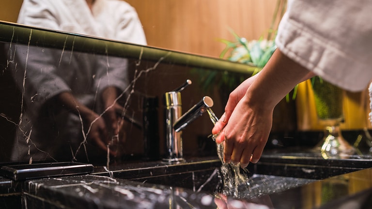 Kobieta myje ręce w pokoju hotelowym – obiekt zapewnia gościom komfort, stabilne ciśnienie wody, a woda ciepła dostępna jest natychmiast