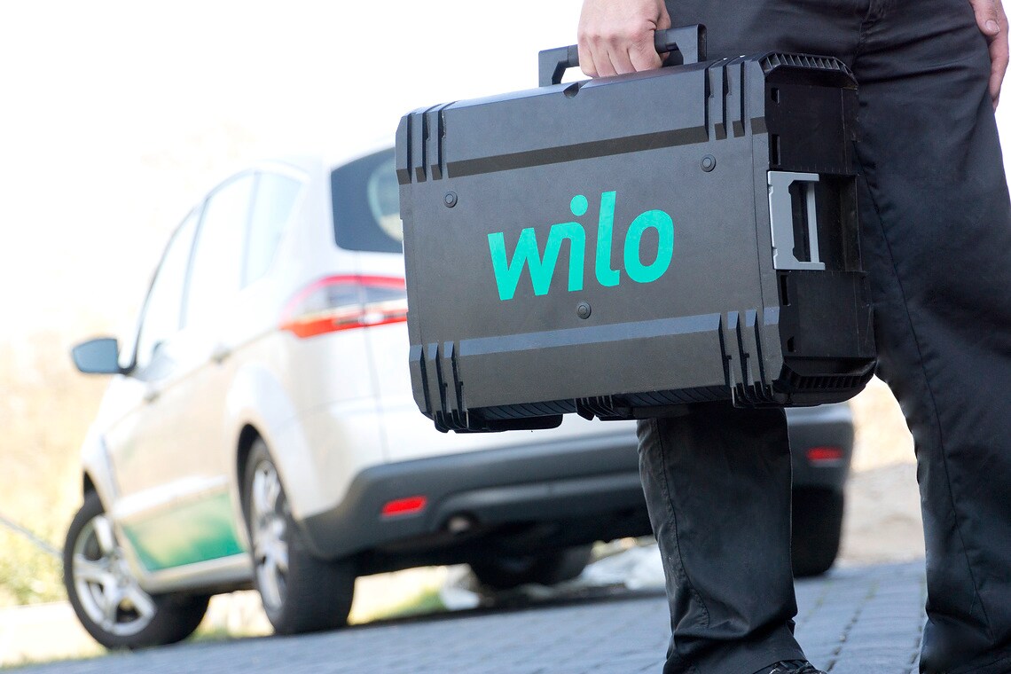 Service technician (Mr. Muslu) with a Wilo tool case in his hand, in the background is a Wilo car